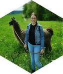 Bild von Heike Kohl in Jeansjacke mit einem braunen Alpaka auf einer grünen Wiese.