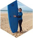 Heike Kohl am Strand im Neopren mit einem großen blauen Surfbrett.